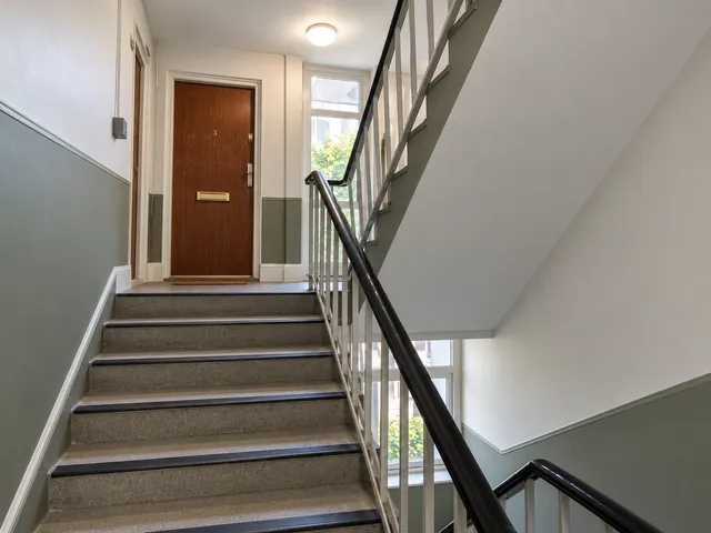 The same stairwell with fresh walls, a green-grey lower half and a black handrail.