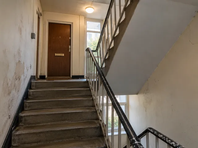 A communal stairwell with damp-stained, peeling walls.